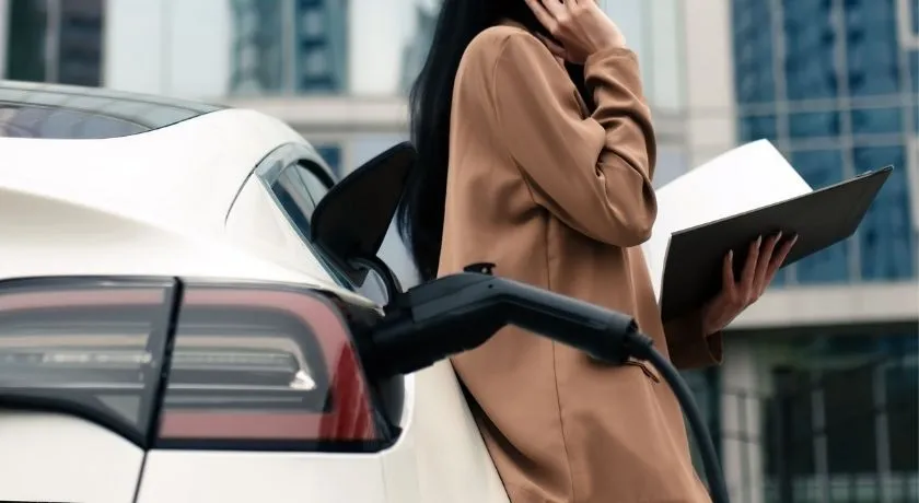 電話をかけているオフィスワーカーが、充電中のEVに寄りかかる